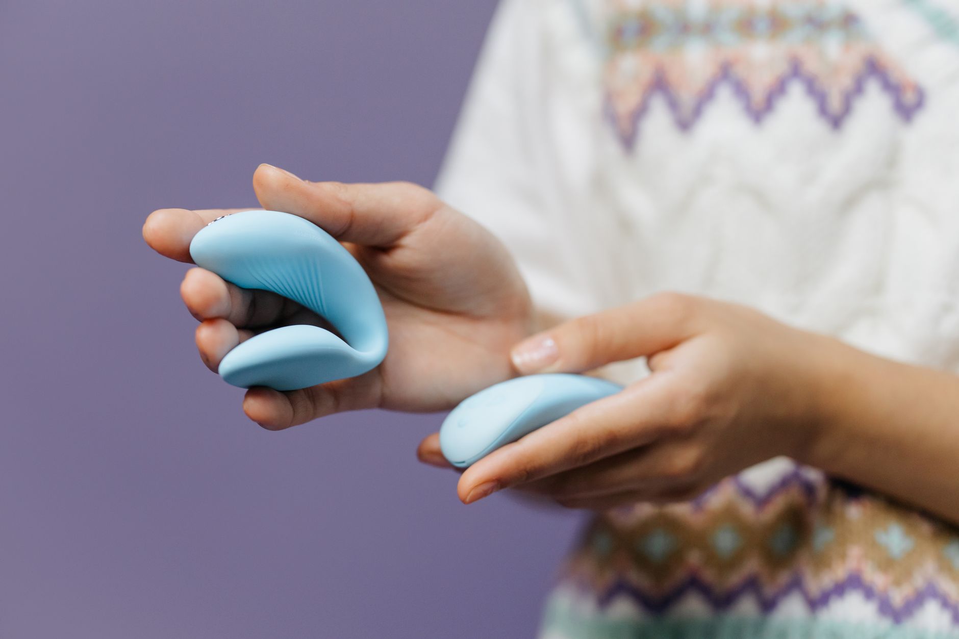Close-up of hands holding a sleek blue vibrator, representing intimate self-pleasure without performance pressure